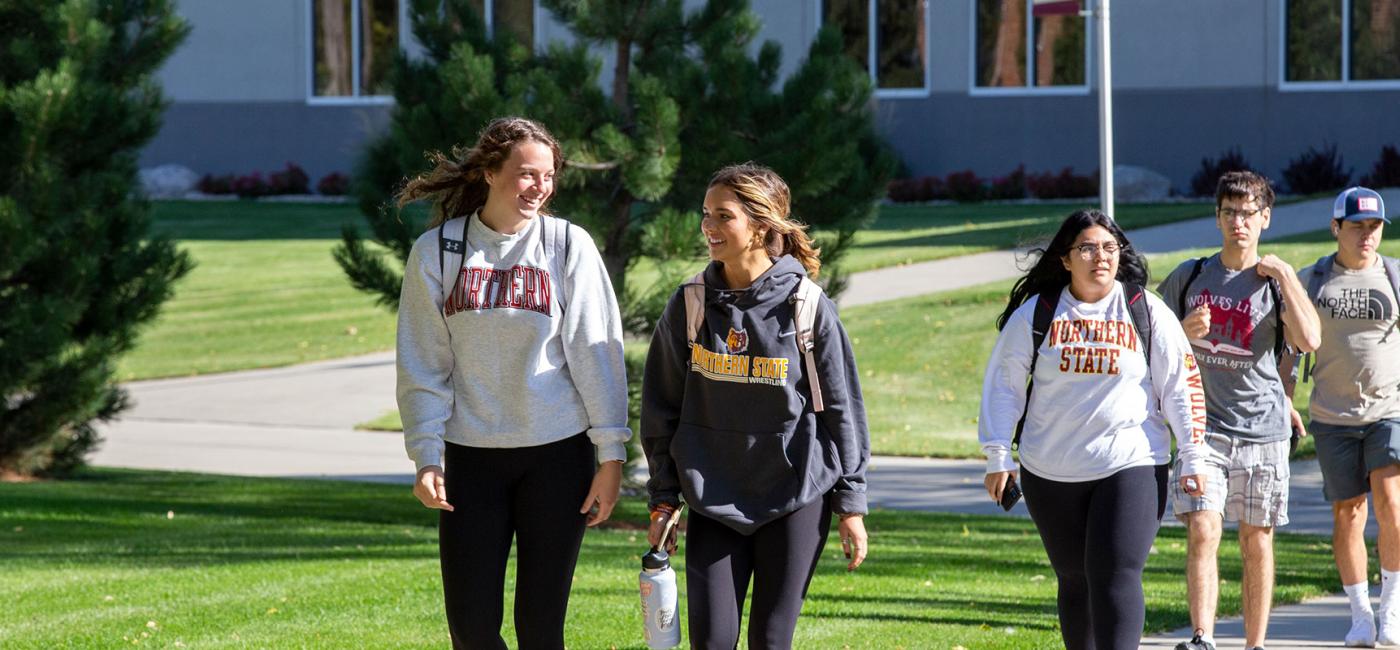 Students in sweatshirts smile at each other as they walk across campus